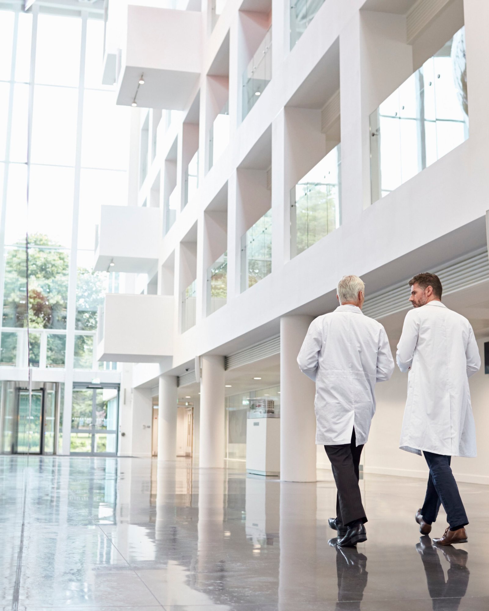 Rear View Of Doctors Talking As They Walk Through Hospital